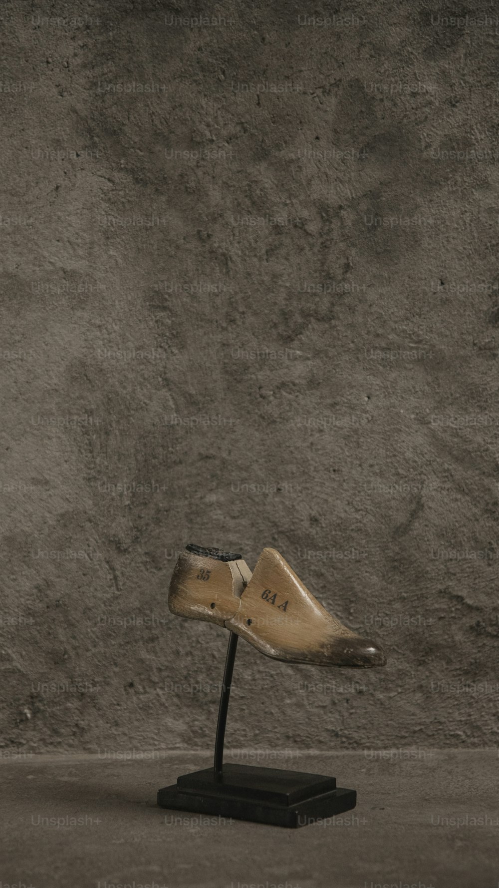 Un zapato de madera en un soporte frente a un muro de hormigón