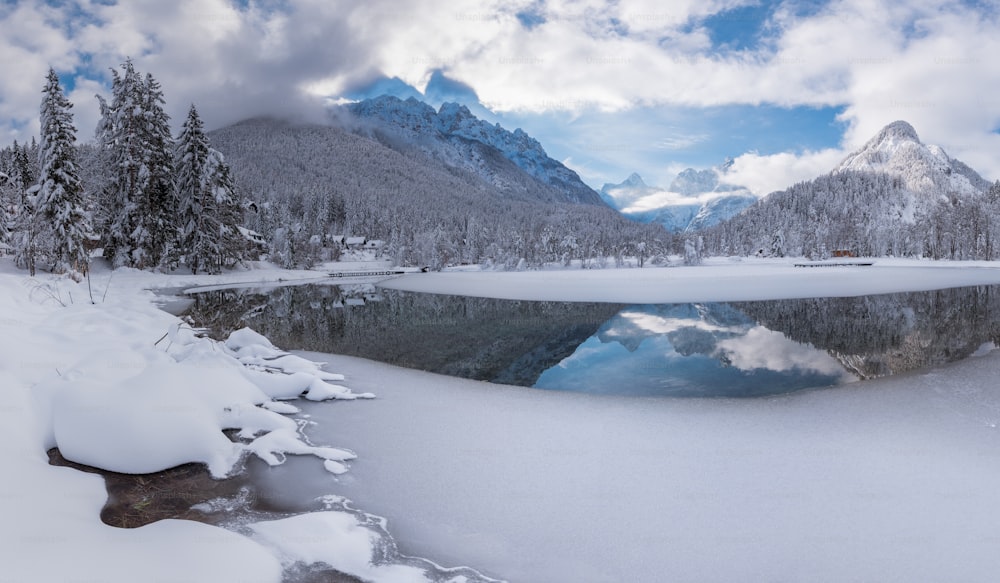 a lake surrounded by snow covered mountains under a cloudy sky