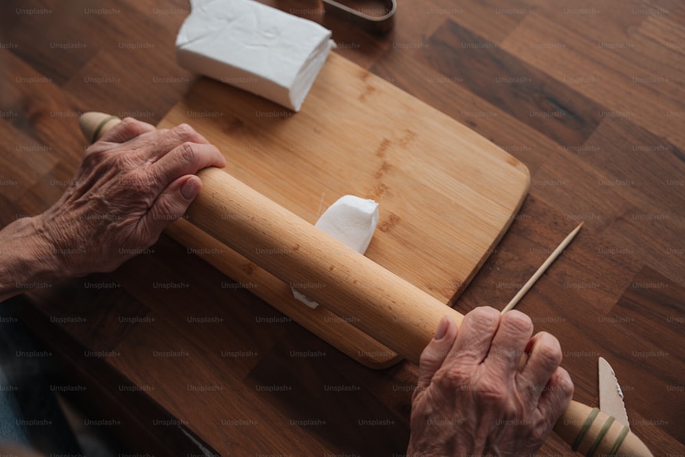 uma pessoa idosa segurando um rolo em cima de uma mesa de madeira