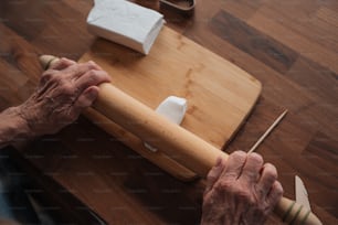 an older person holding a rolling pin on top of a wooden table