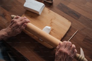 uma pessoa idosa segurando um rolo em cima de uma mesa de madeira