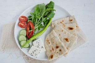 un piatto bianco condito con verdure e pane pita