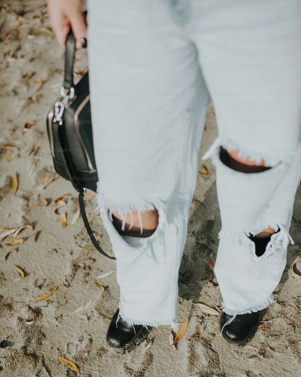 una persona con i jeans strappati che tiene una borsa