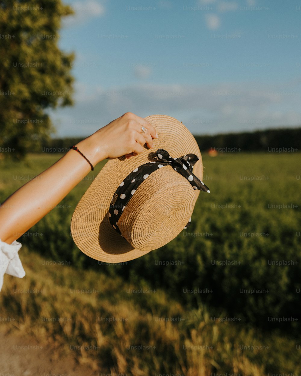 a woman's hand holding a straw hat in front of a field