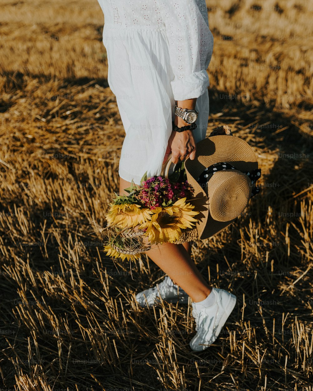 Une femme en robe blanche tenant un bouquet de tournesols