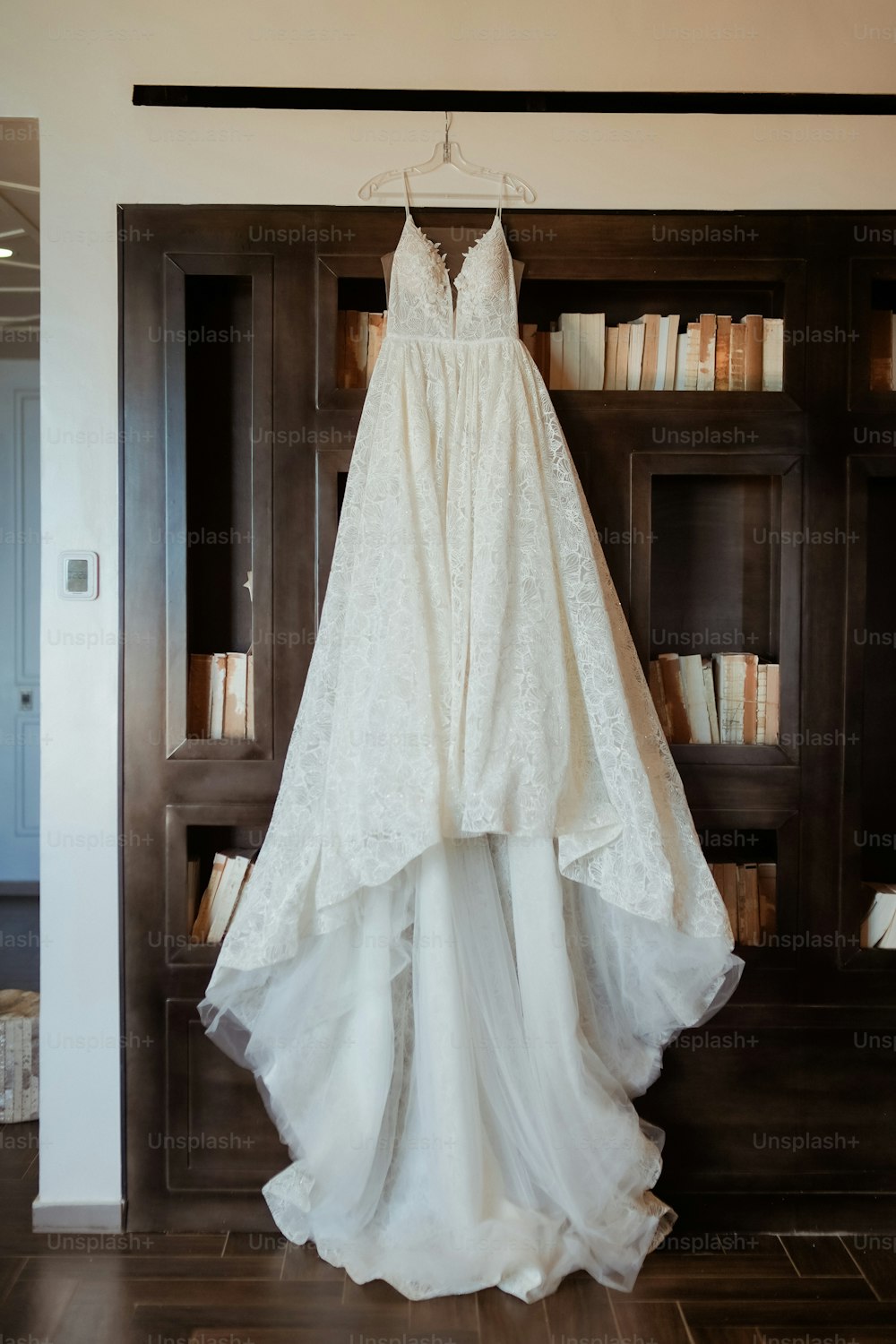 a wedding dress hanging in front of a bookcase