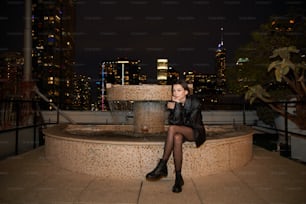 a woman sitting on a ledge in front of a fountain