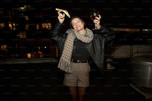 a woman holding a glass of wine and a piece of pizza