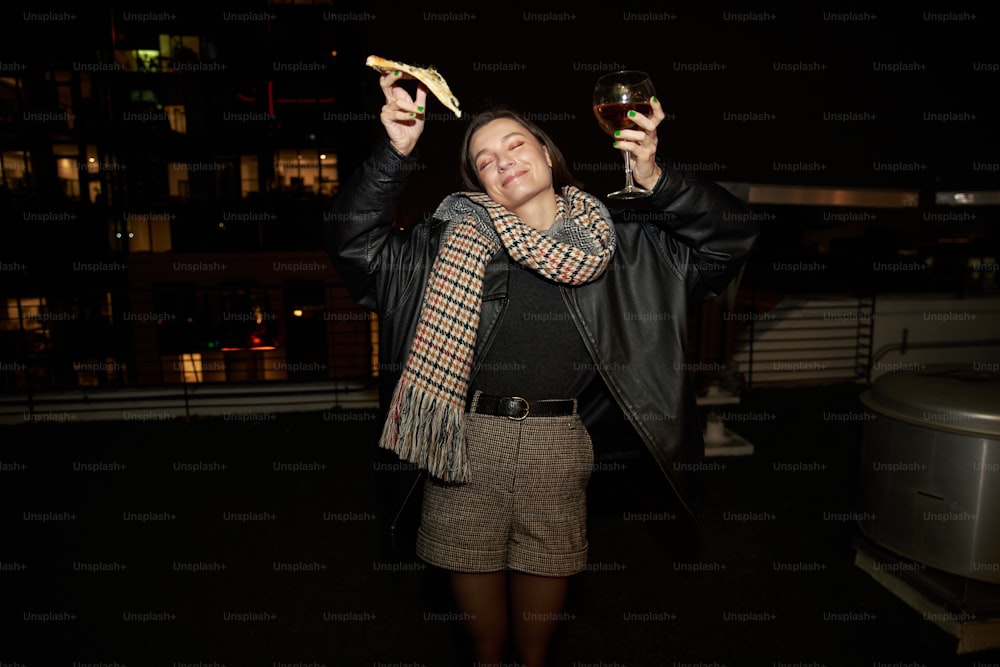 a woman holding a glass of wine and a piece of pizza