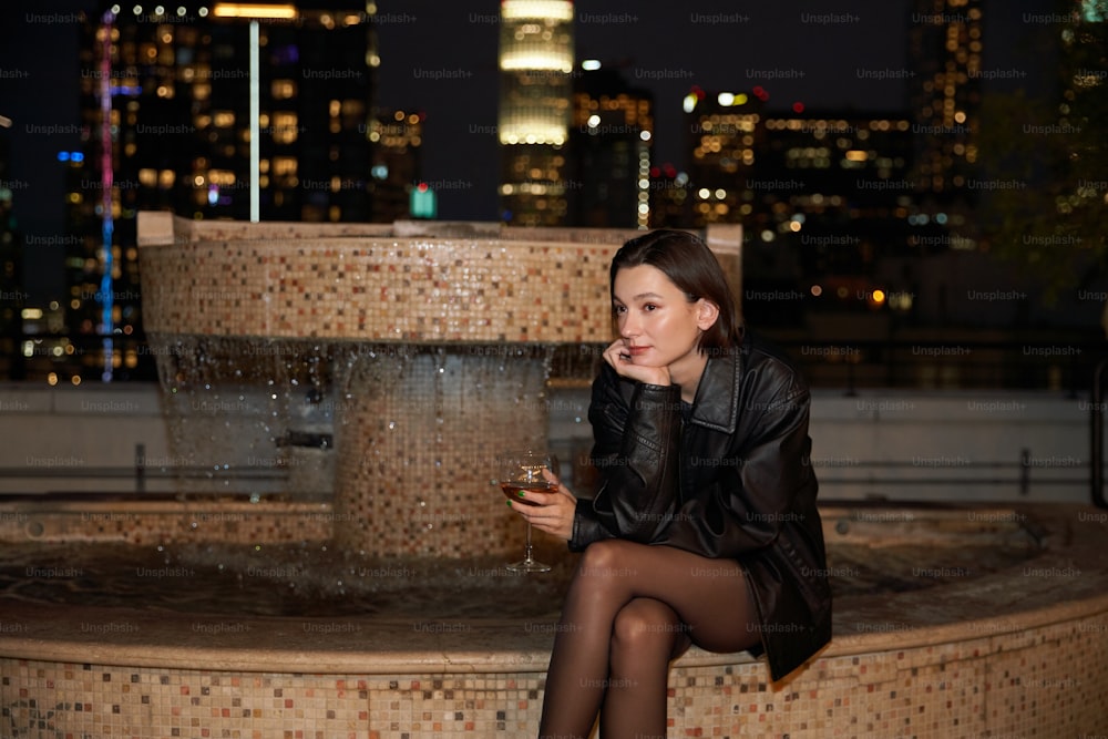 a woman sitting on a fountain drinking a glass of wine