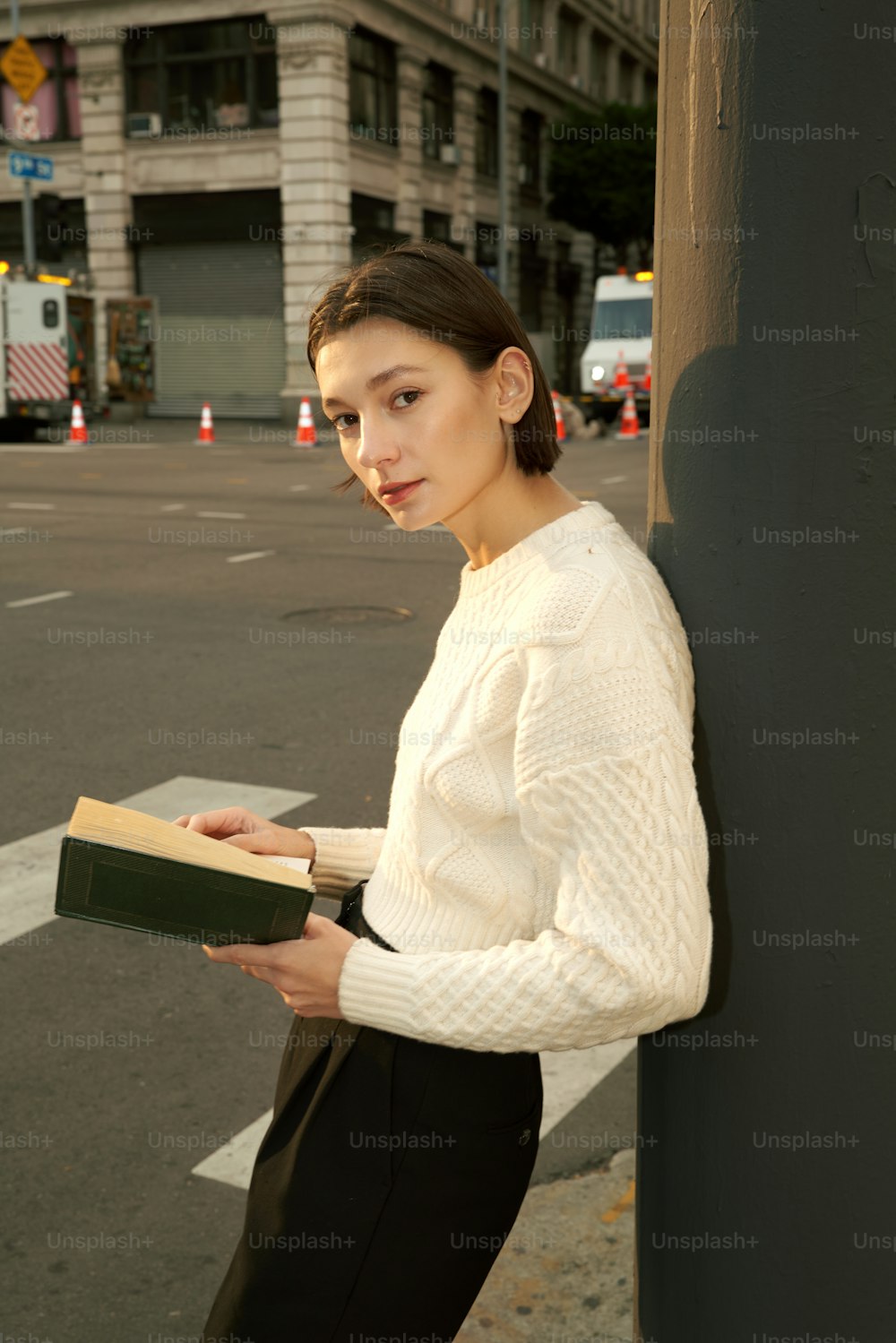 Una mujer apoyada contra un poste mientras sostiene un libro