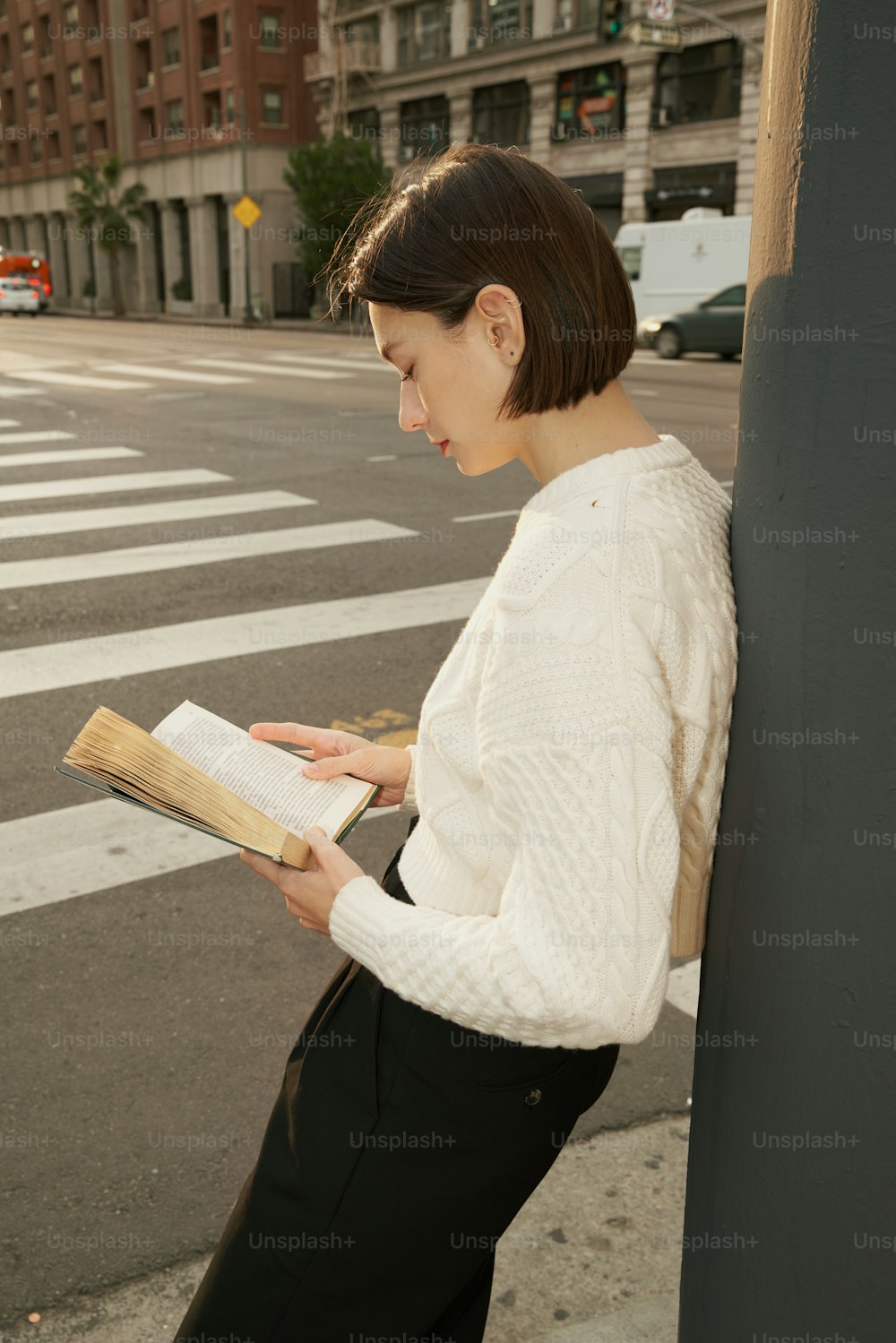Una mujer apoyada contra una pared leyendo un libro