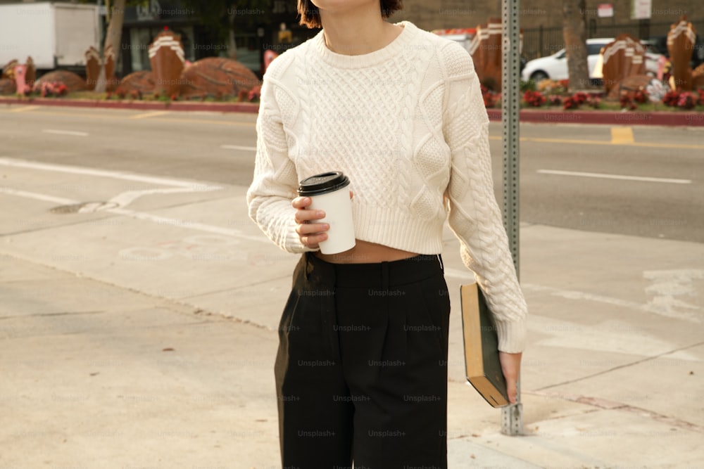 a woman standing on a sidewalk holding a cup of coffee