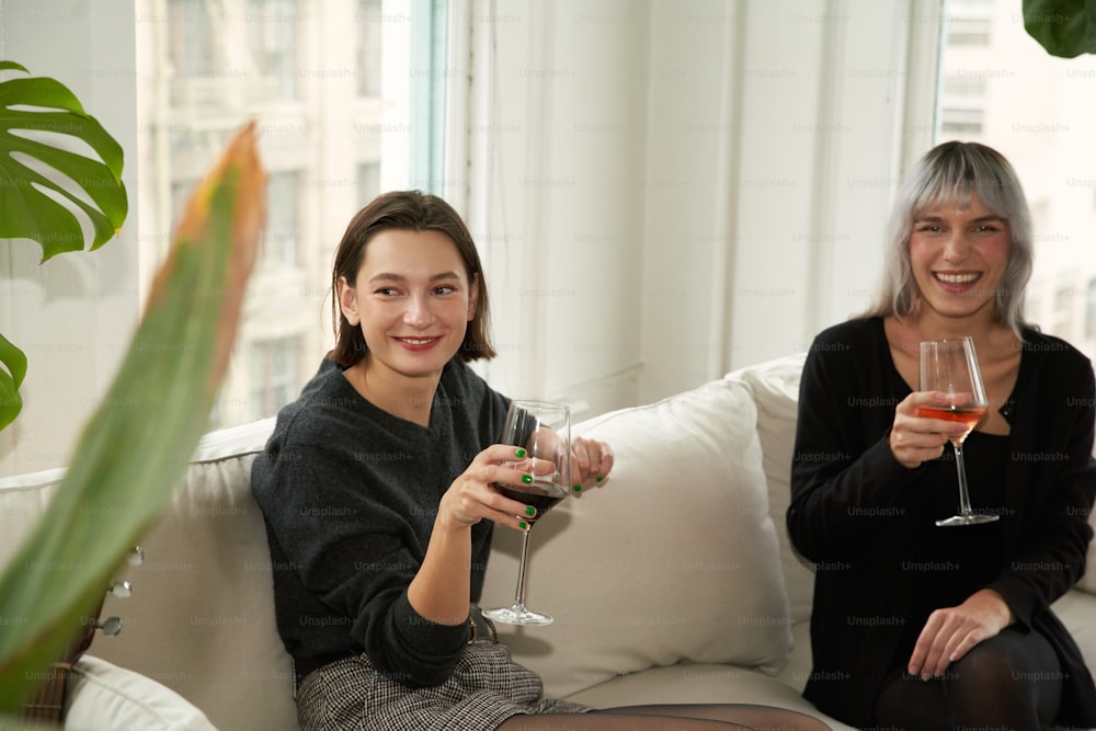 two women sitting on a couch holding wine glasses