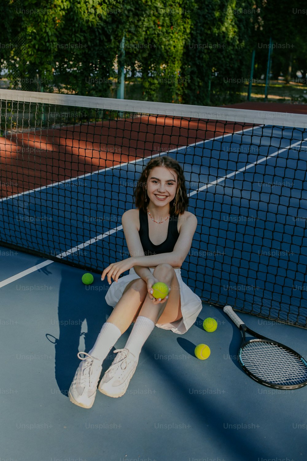 a woman sitting on a tennis court holding a tennis racket
