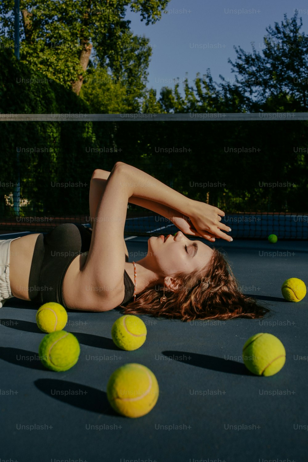 テニスボールに囲まれたテニスコートに横たわる女性