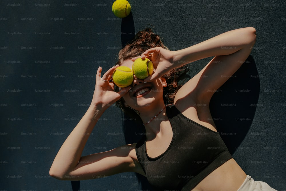 Une femme tenant deux balles de tennis devant son visage