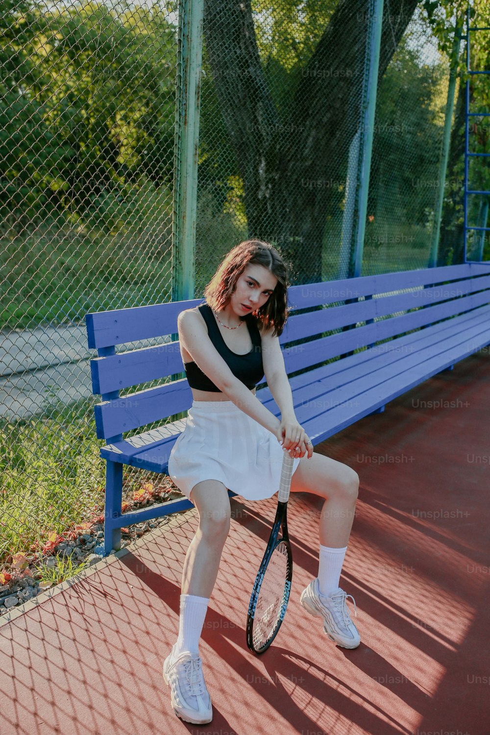 Una mujer sentada en un banco sosteniendo una raqueta de tenis