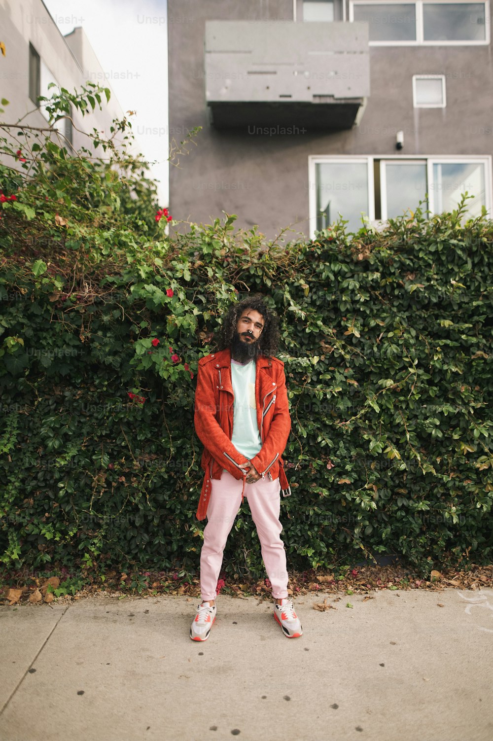 a man with a beard standing in front of a hedge