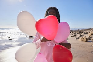 a woman on the beach holding a bunch of balloons