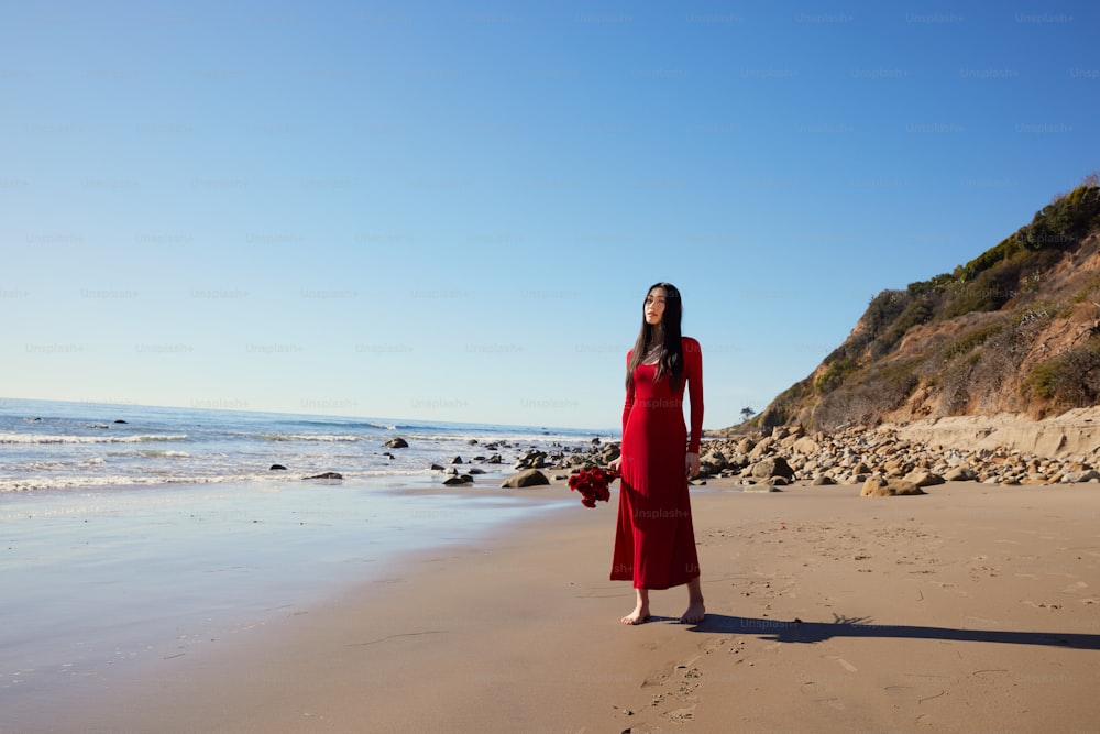 a woman in a red dress standing on a beach