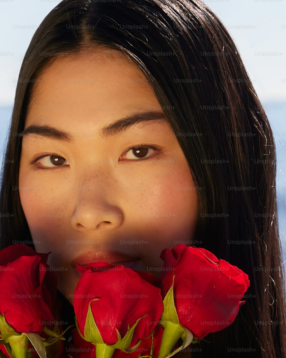 a woman with long black hair holding roses in her mouth