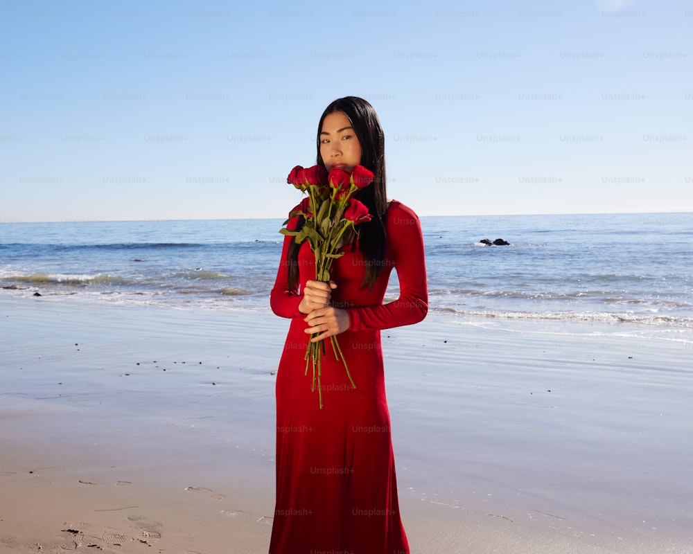 a woman standing on a beach holding a bouquet of flowers