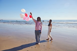two women standing on a beach holding balloons