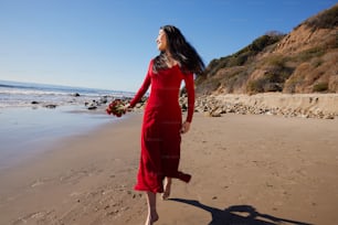 a woman in a red dress is walking on the beach