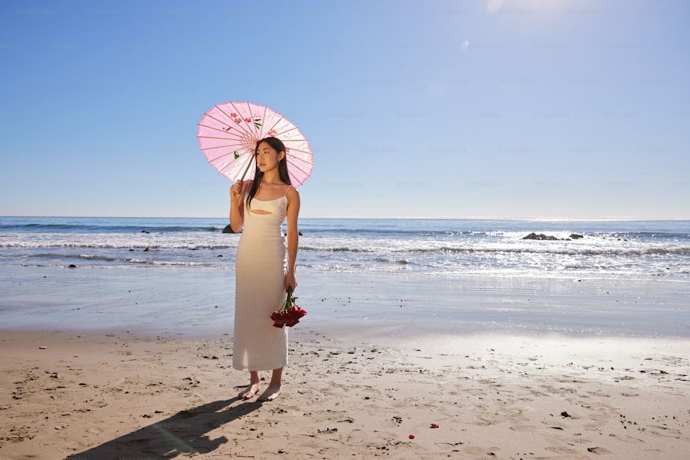 a woman standing on a beach holding a pink umbrella