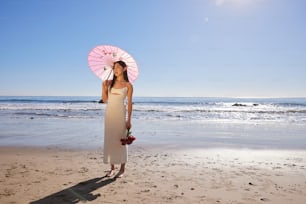 a woman standing on a beach holding a pink umbrella