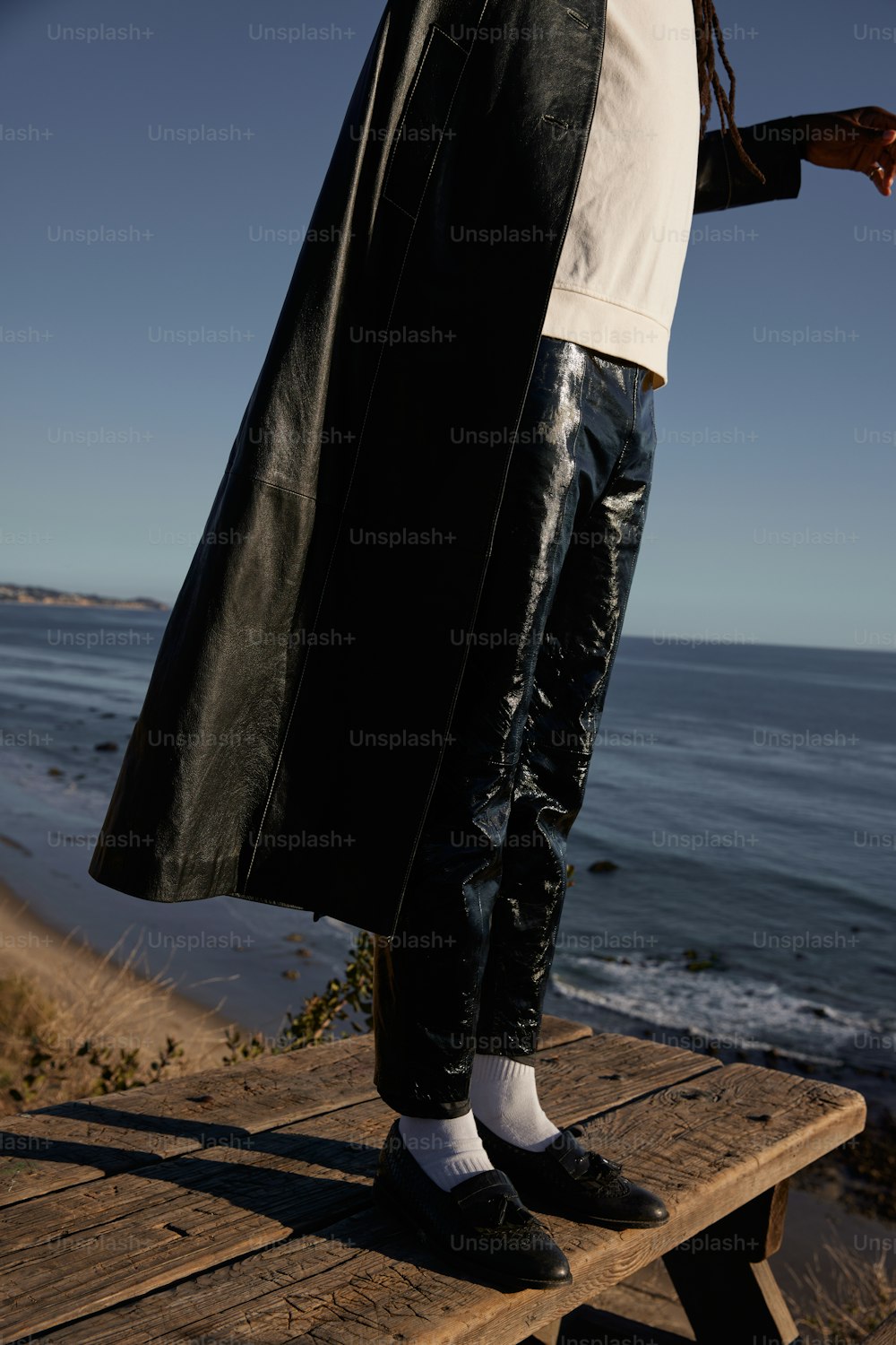 a man standing on a wooden bench near the ocean