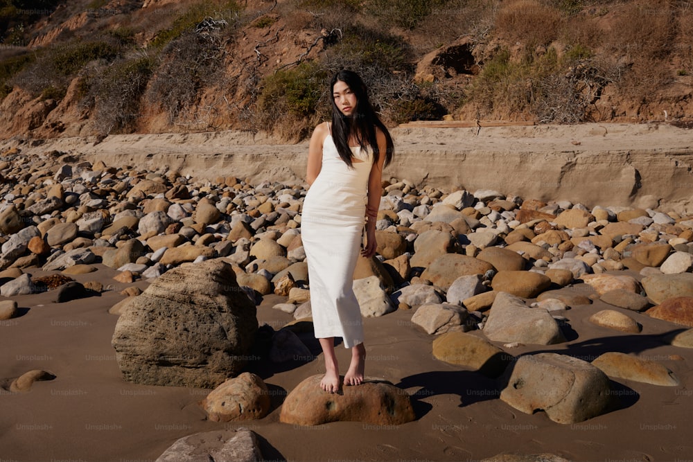 a woman in a white dress standing on a rocky beach