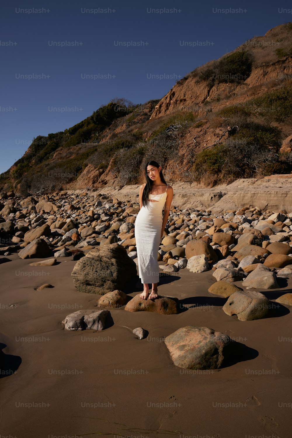 a woman in a white dress standing on a rocky beach