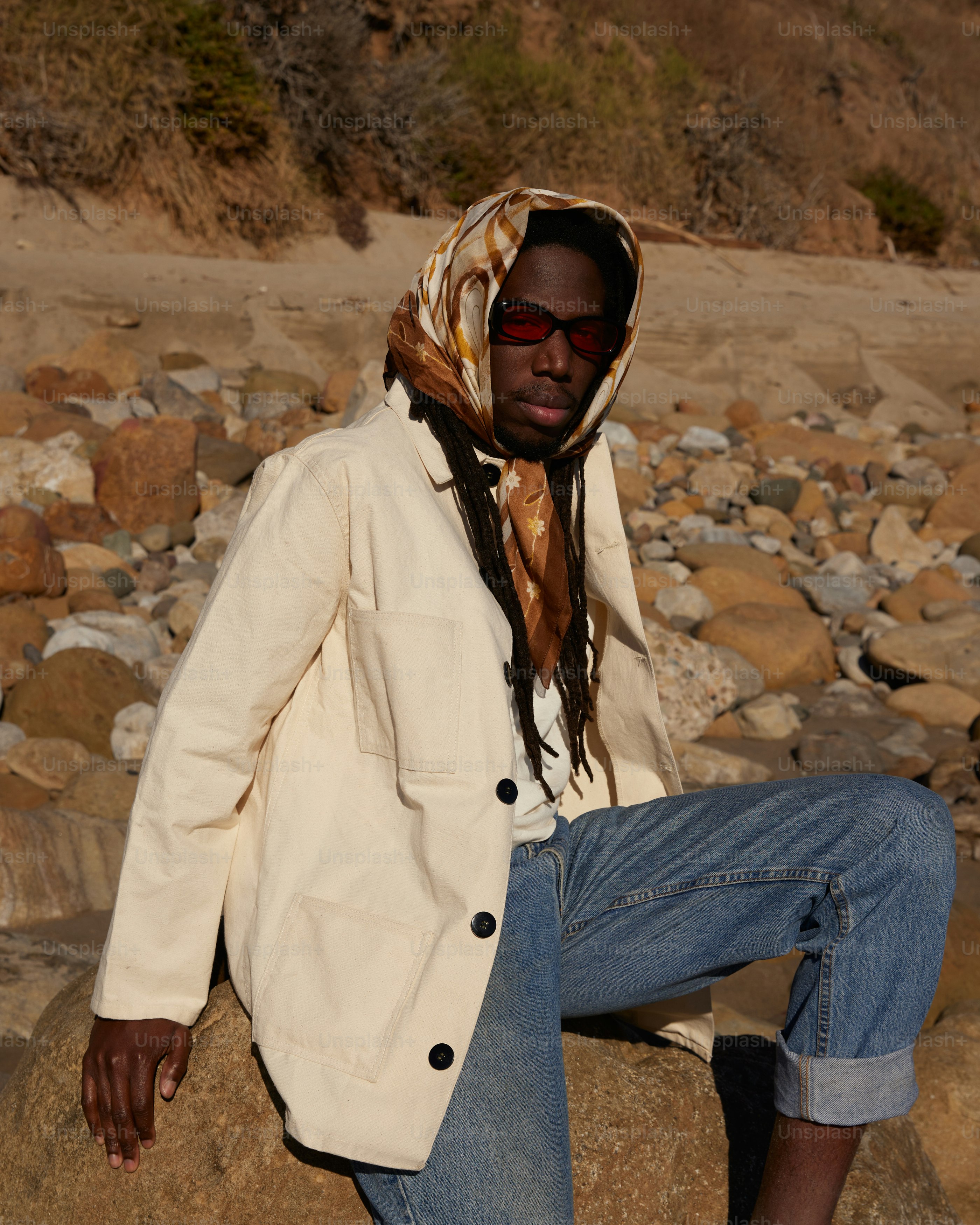 a man sitting on a rock with a scarf around his head