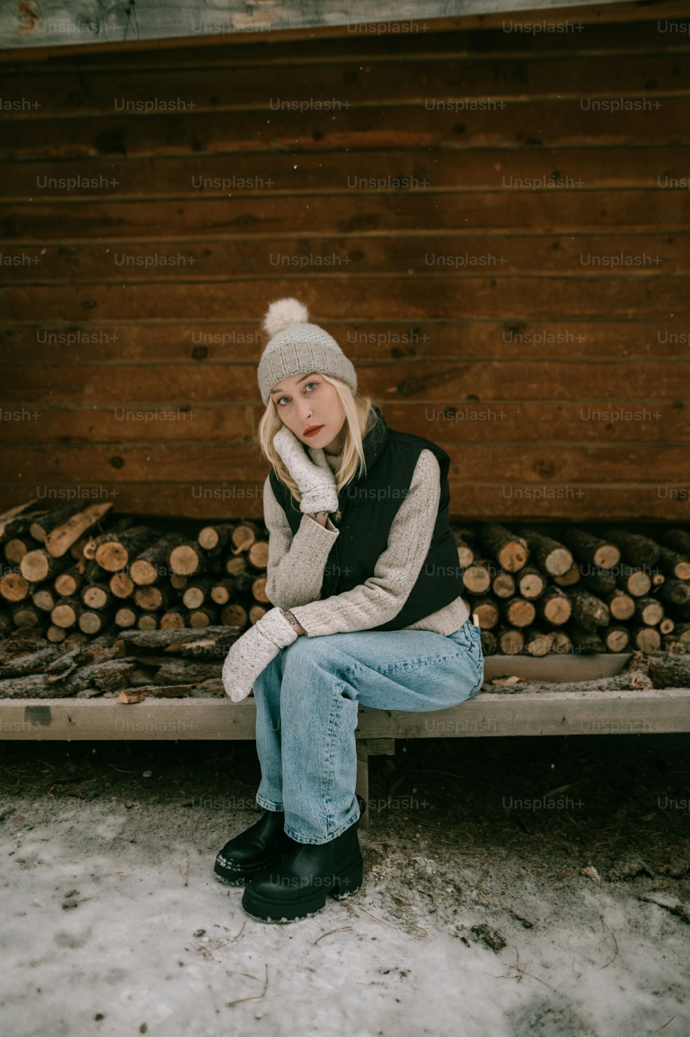 a woman sitting on a bench in front of a pile of logs