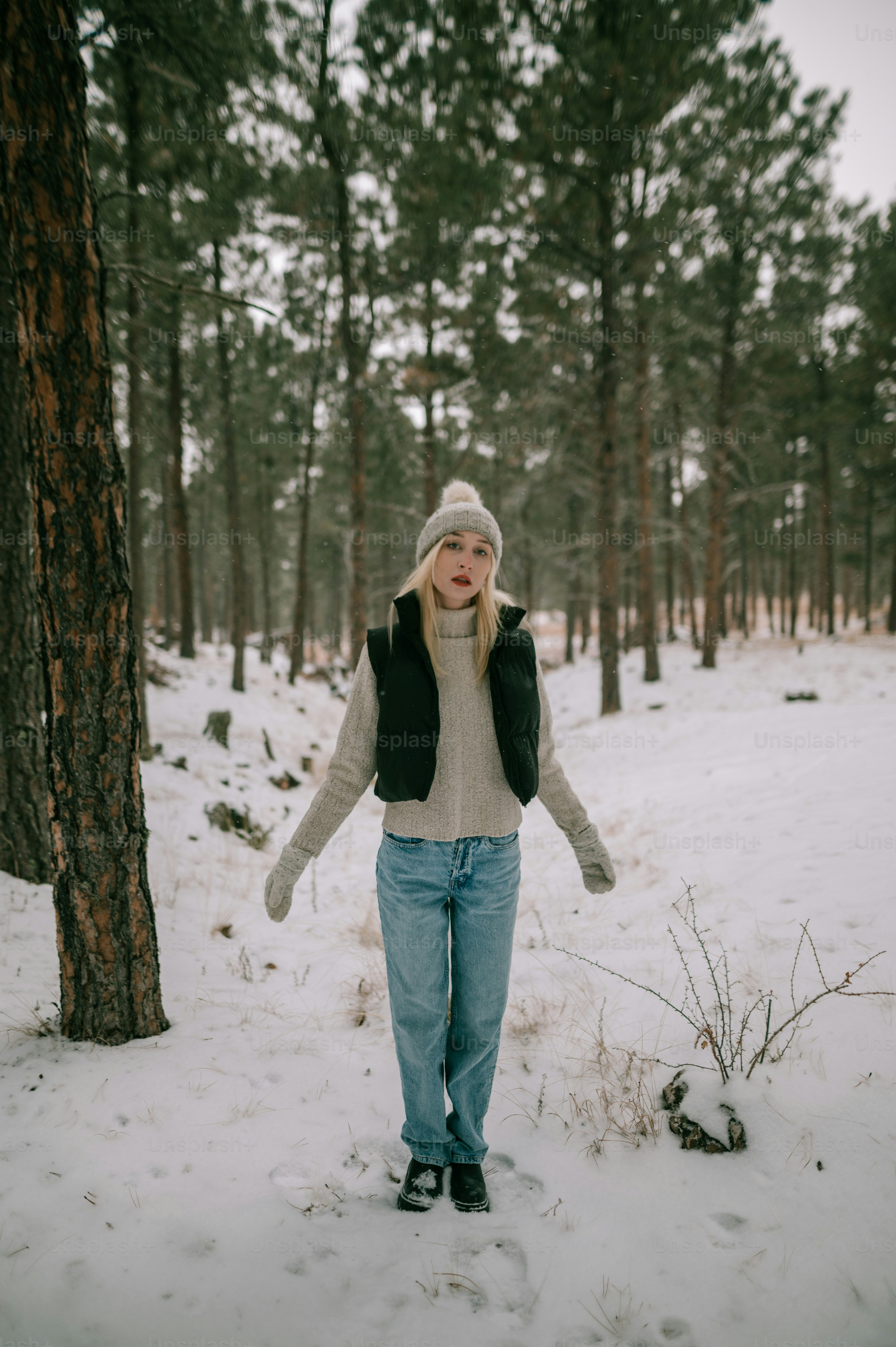 a woman standing in the snow next to a tree