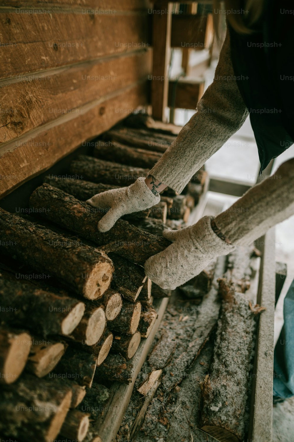 a person holding a pair of gloves over a pile of logs