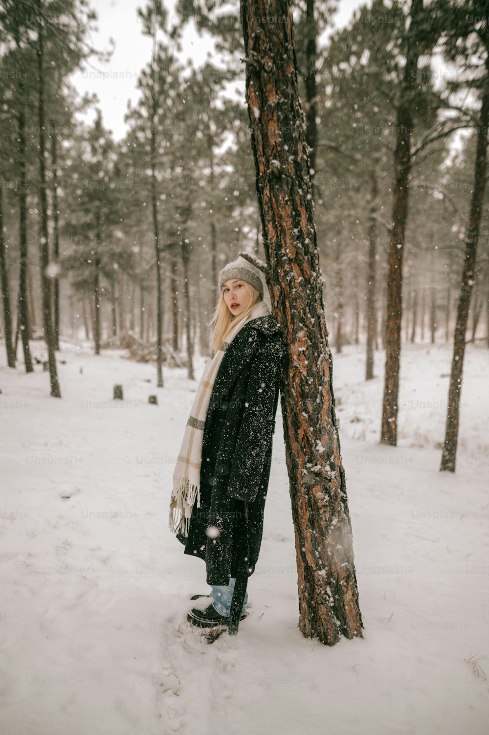 a woman standing next to a tree in the snow