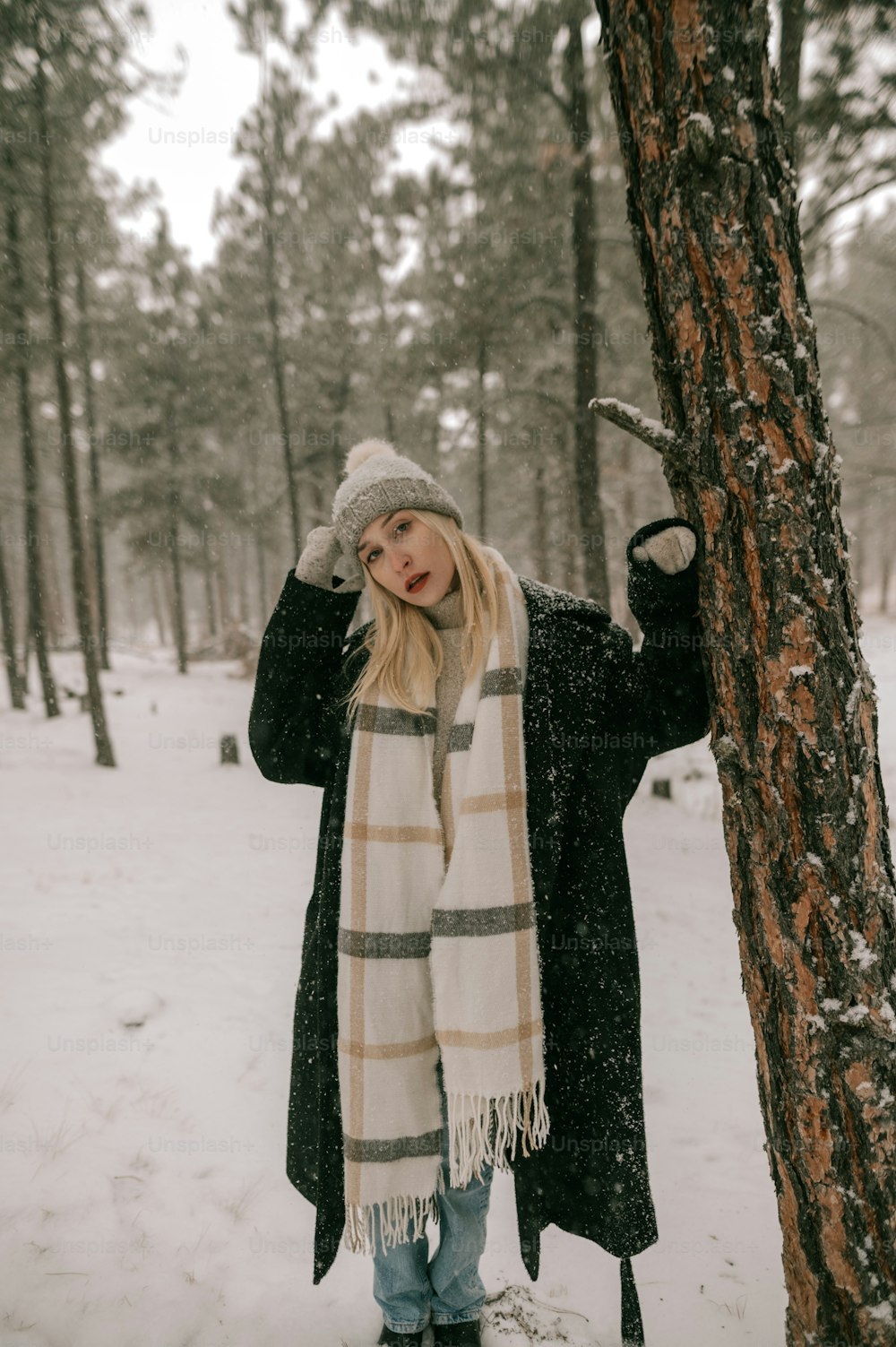 a woman standing next to a tree in the snow