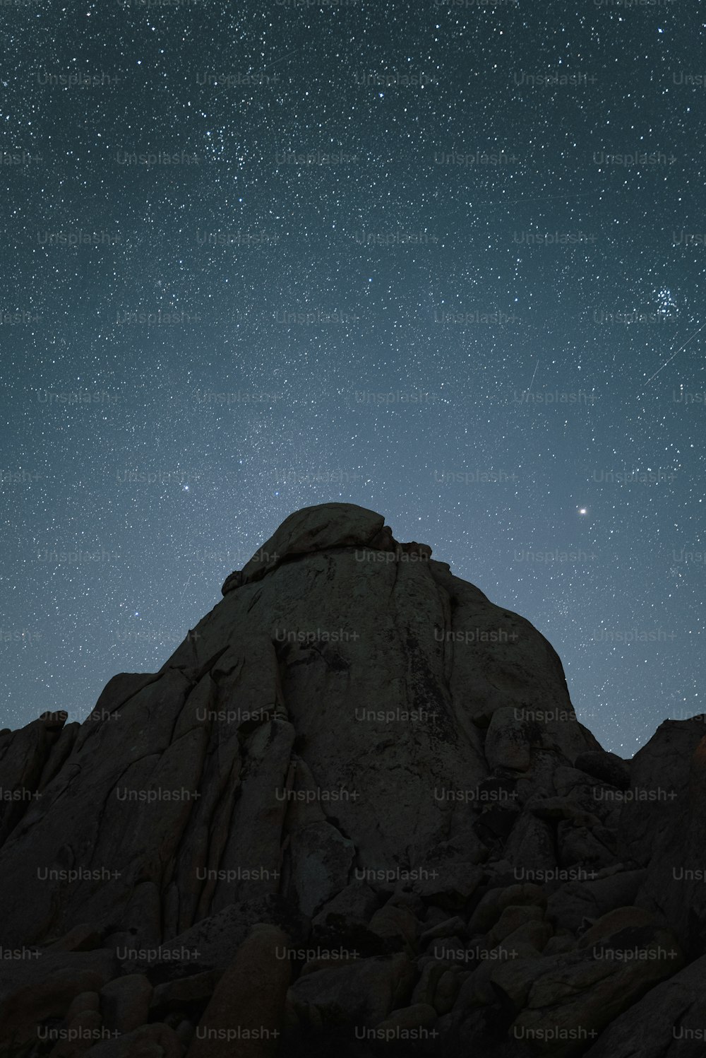 the night sky with stars above a rocky mountain
