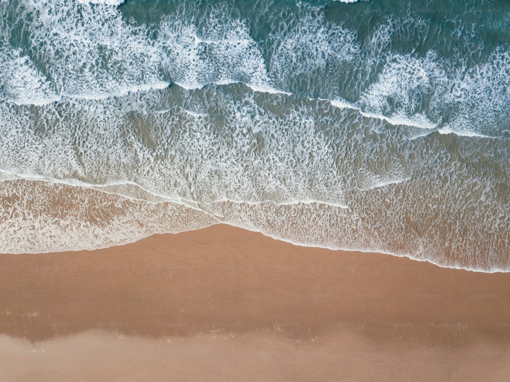 an aerial view of a sandy beach with waves