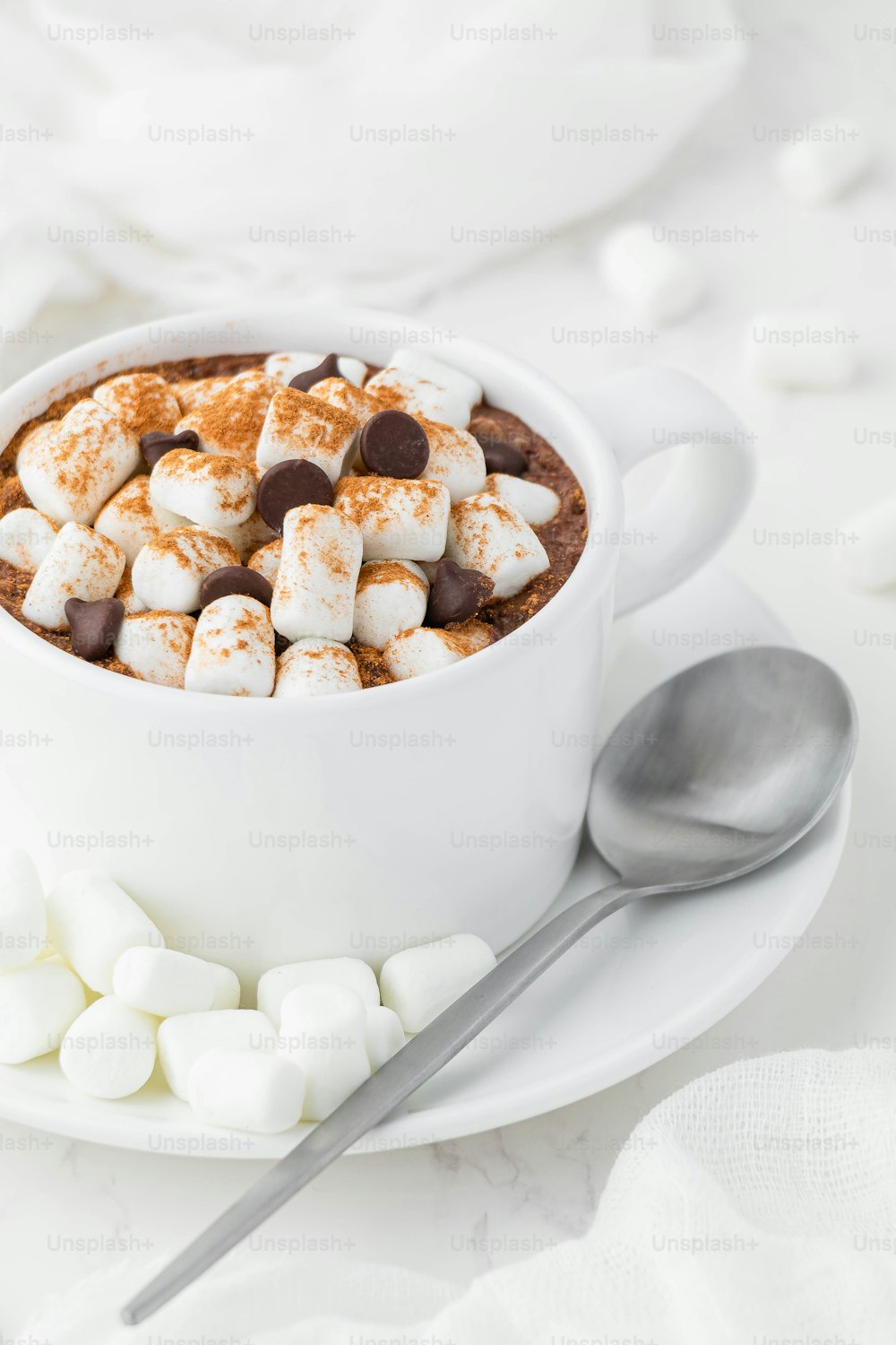 uma xícara de chocolate quente com marshmallows e uma colher