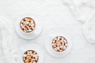 three cups of hot chocolate topped with marshmallows