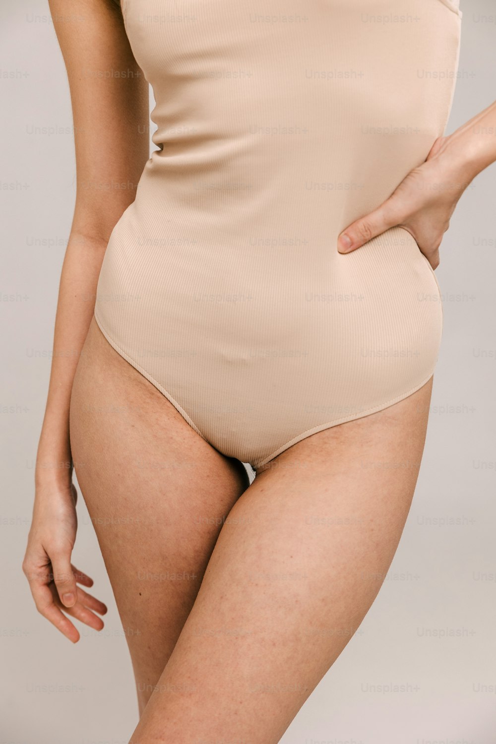 a woman in a tan bodysuit with her hands on her hips