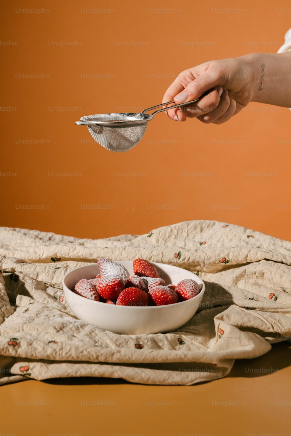 a bowl of strawberries on a table with a person holding a spoon