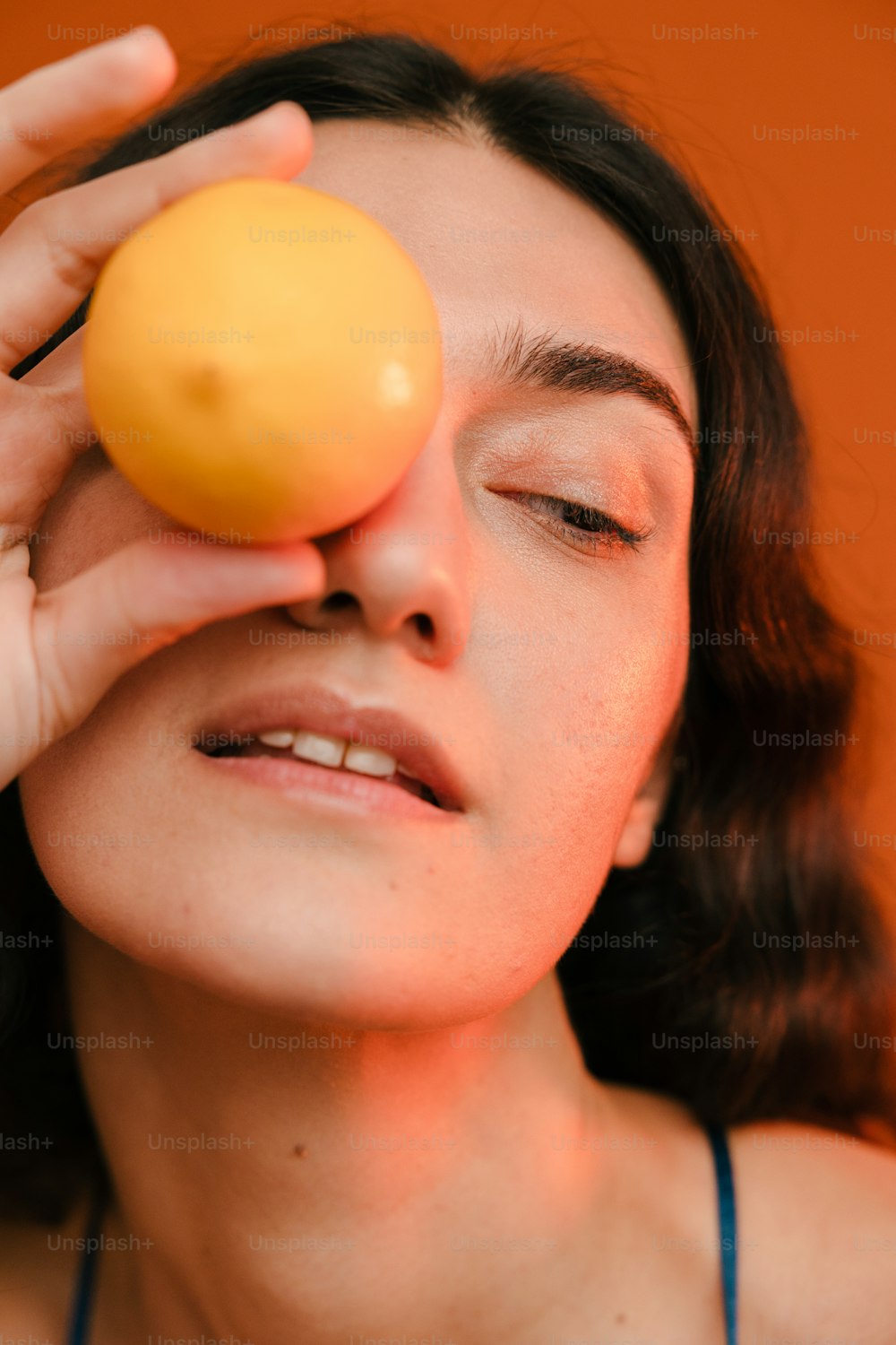 a woman holding an orange up to her eye