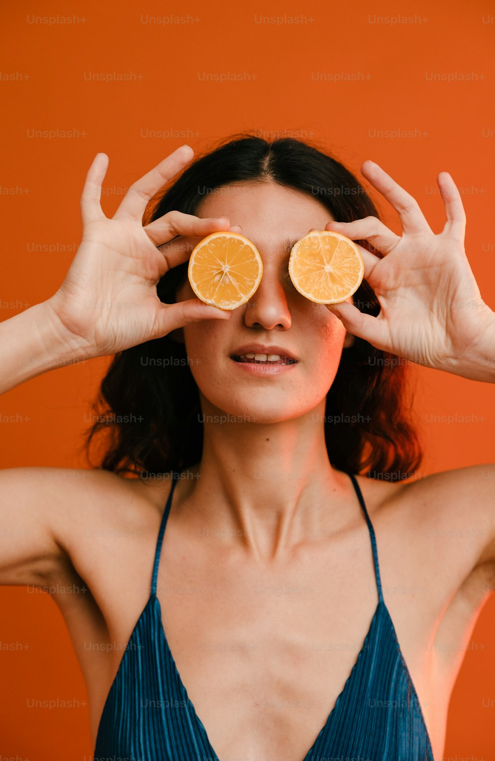 Une femme tenant deux tranches d’oranges devant ses yeux