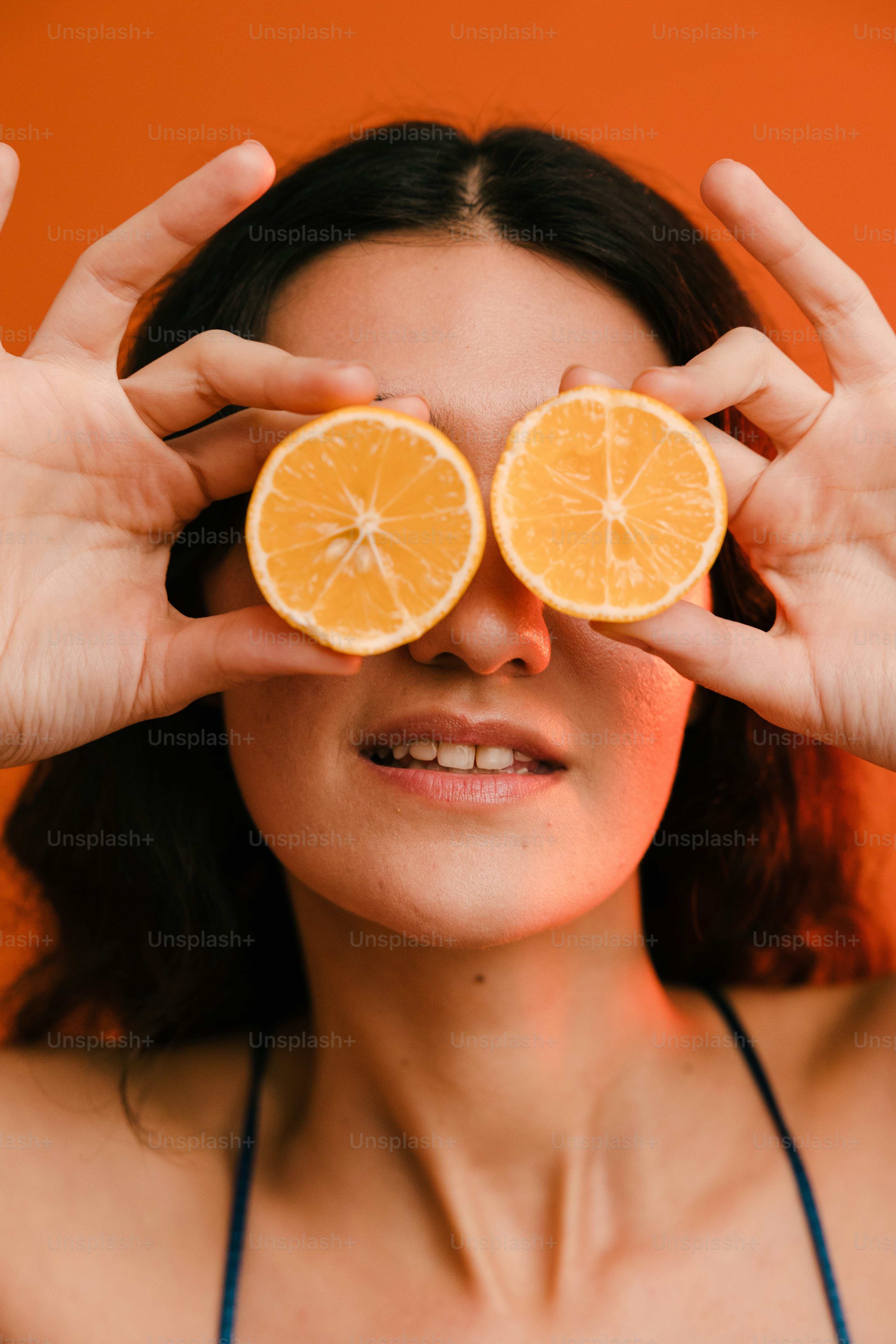 a woman holding two slices of oranges in front of her eyes