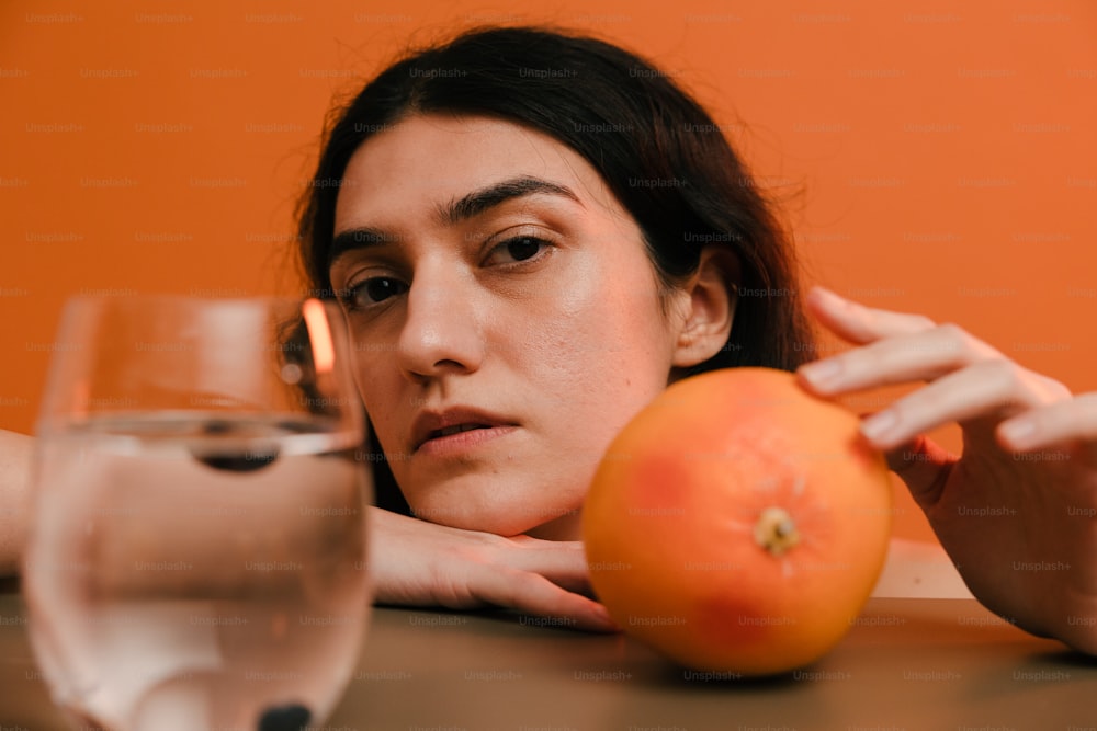 a woman sitting at a table with an orange and a glass of water